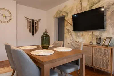 a dining room table with chairs and a television on a wall at Apartman Nest in Vranje