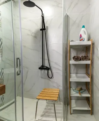 a shower with a glass door and a stool in a bathroom at Apartman Nest in Vranje