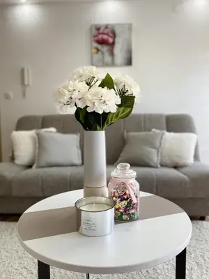 a white vase with white flowers on a table at La Perla Apartman in Vrnjačka Banja