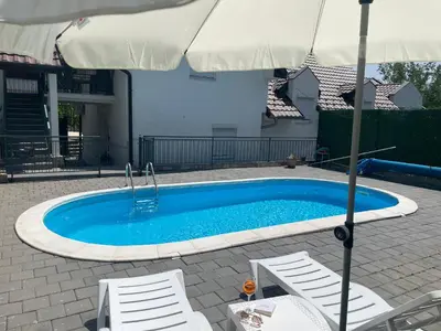 a swimming pool with two chairs and an umbrella at La Perla Apartman in Vrnjačka Banja