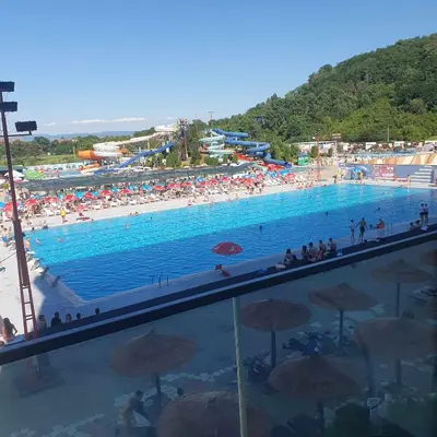 a large swimming pool with a beach with people and umbrellas at Aqua Lux Apartman in Jagodina