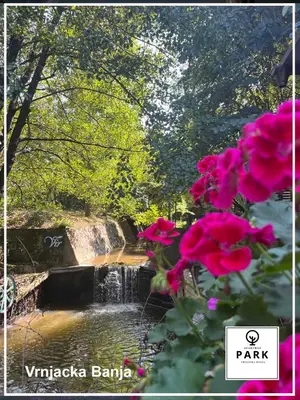 a waterfall in a park with pink flowers in the foreground at Apartman Park Promenada in Vrnjačka Banja