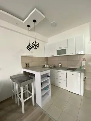 a kitchen with white cabinets and a table and stool at Aqua Panoramic Apartments in Jagodina