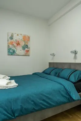 a bedroom with a blue bed with a painting on the wall at Apartman Ina in Vrnjačka Banja