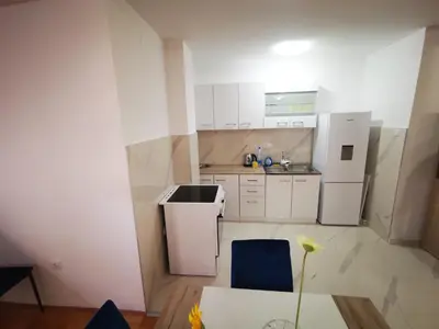 a small kitchen with white cabinets and a blue chair at Riviera Apartments in Niš