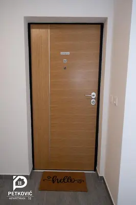 a wooden door with a welcome mat in front of it at Petković apartmani STUDIO32 in Jagodina