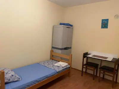a small room with a bed and a desk with a refrigerator at Hostel Drenak in Gornje Rataje