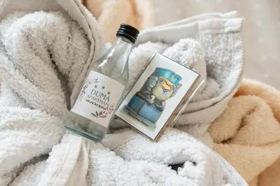 a bottle of alcohol and a book on a towel at Duma Apartmani 1 Vrnjačka Banja in Vrnjačka Banja