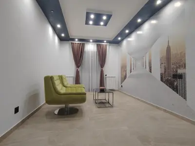 a living room with a green chair and a staircase at Hedonic Wellness Apartmani in Niš