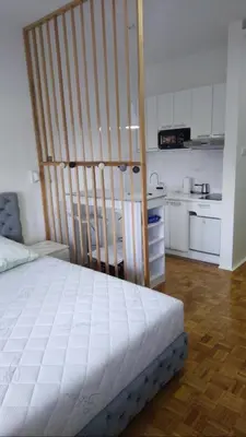 a bedroom with a white bed and a kitchen at AIK Kula studio in Jagodina