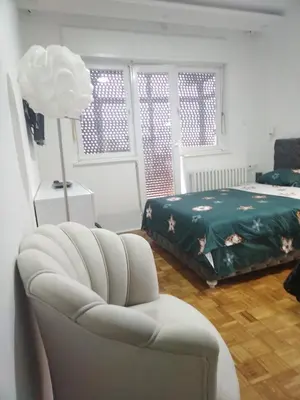 a living room with a white chair and a bed at AIK Kula studio in Jagodina