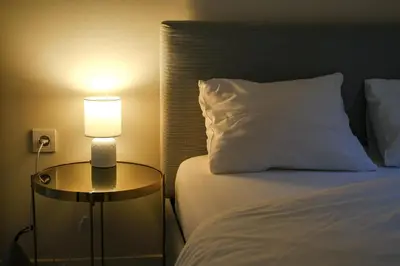 a bed with a white pillow and a table with a lamp at Apartment in Niš, Center! brand-new in Niš