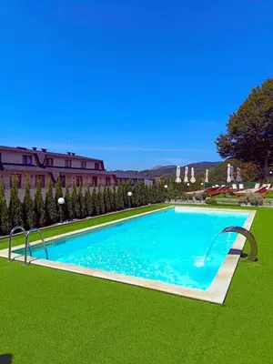 a large swimming pool with green grass next to a building at Kloudscape Apartman Milmari Resort & Spa in Kopaonik