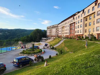 a building on a hill next to a street with cars at Kloudscape Apartman Milmari Resort & Spa in Kopaonik