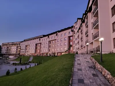 a large building with a grassy field in front of it at Kloudscape Apartman Milmari Resort & Spa in Kopaonik