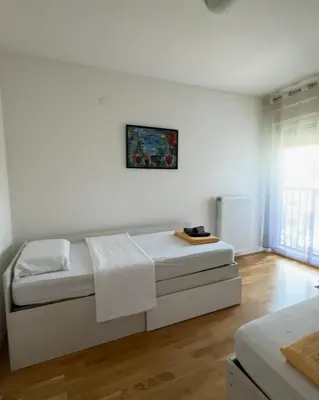 a white bedroom with a bed and a picture on the wall at Niš East gate APT with balcony and free private Parking in Donja Vrežina