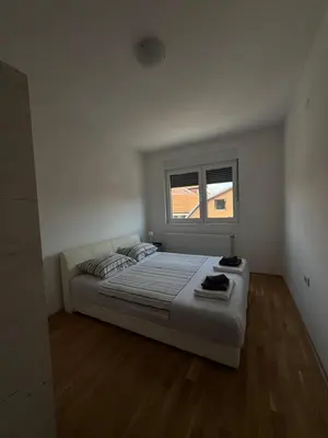 a white bedroom with a large bed and a window at Niš East gate APT with balcony and free private Parking in Donja Vrežina