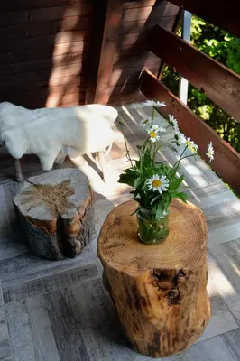 a sheep standing on a porch with two logs and a vase of flowers at Cabin & Apartment Kopaonik in Kopaonik