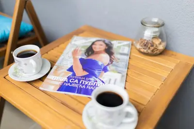 a table with two cups of coffee and a magazine at Apartman Iris in Niš