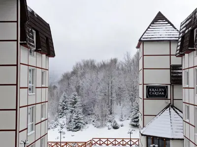 a view of a snow covered forest from between two buildings at Apartman KUTIJA Kopaonik in Kopaonik