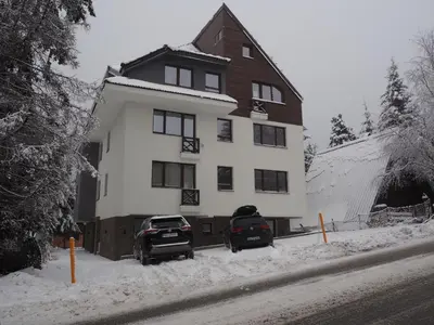 two cars parked in front of a house in the snow at Apartman Duda in Kopaonik