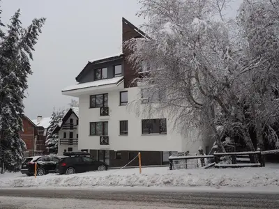 a snow covered building with cars parked in front of it at Apartman Duda in Kopaonik