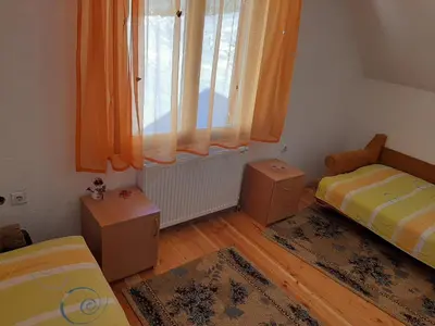 a bedroom with two beds and a window with orange curtains at Vikend kuća Vukašinović in Kopaonik