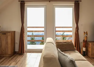 a living room with a couch and two large windows at Vila Kruna Sunčani Breg in Kopaonik