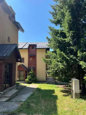 a house with a tree next to a building at Apartman Treska Kop in Kopaonik