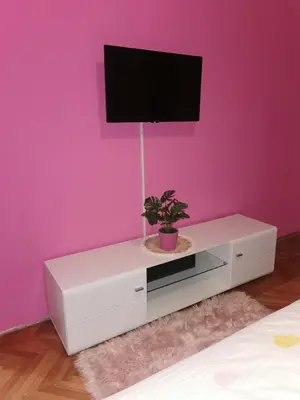 a white dresser with a tv on a pink wall at Apartman Aki in Pirot