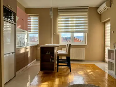 a kitchen with a table and a chair and two windows at Trident Apartments 3 in Niš