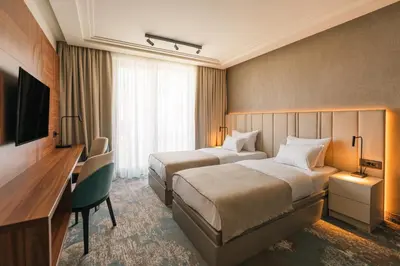 a hotel room with two beds and a desk and a television at Hotel Kocka Vrnjačka Banja in Vrnjačka Banja