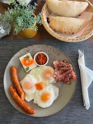 a plate of eggs bacon sausage and bread on a table at Triangle Rooms in Raška