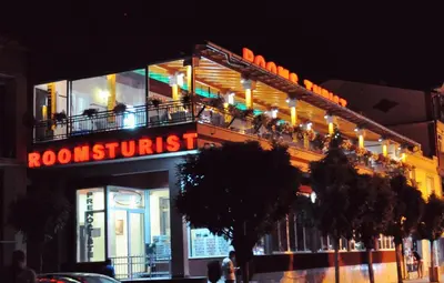 a building with a sign for a restaurant with people on the balcony at Rooms Turist in Vladičin Han