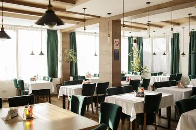 a restaurant with white tables and chairs and windows at Pukikop Apartman in Kopaonik