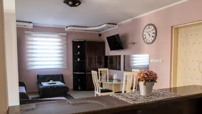 a living room with a table and a clock on the wall at Apartman Lara in Kuršumlija