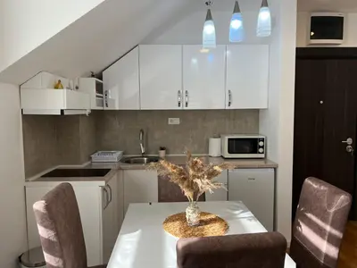 a kitchen with white cabinets and a table with chairs at Milka apartman Sokobanja in Soko Banja