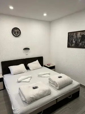 a bedroom with a bed with white sheets and a clock on the wall at Apartmani Knez in Kruševac