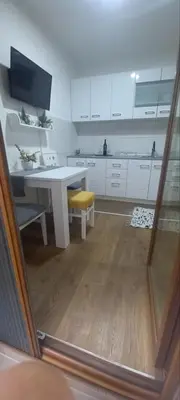 a white kitchen with a table and a yellow stool at Apartman Mila 23 Vrnjačka Banja in Vrnjačka Banja