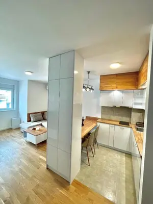 a kitchen and living room with white cabinets and a table at Tina Apartman Sokobanja in Soko Banja