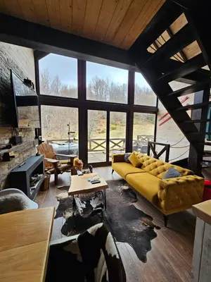 a living room with a yellow couch and a large window at Ski & Spa Bungalows in Kopaonik