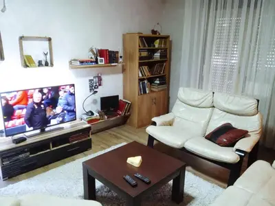 a living room with a white chair and a tv at LUX Apartman in Leskovac