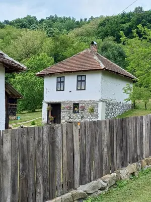 a white house behind a wooden fence at Seosko Domaćinstvo Jevtić in Ždraljica