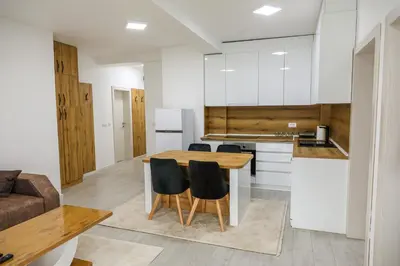 a kitchen with white cabinets and a wooden table and chairs at Apartman Jelena in Vranje