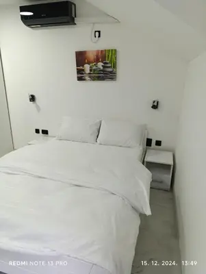 a bed with white sheets and a picture on the wall at Garfield Family Apartman 1 in Soko Banja