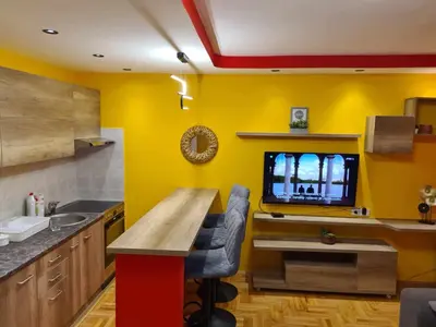 a kitchen with yellow walls and a table and a tv at Stan na dan Braca in Niš