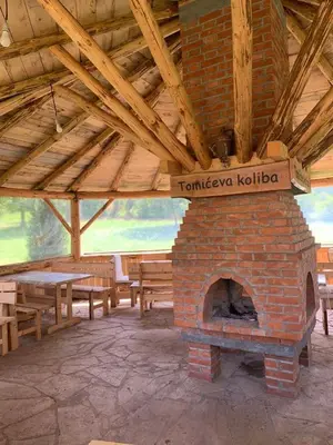 a brick fireplace in a room with tables and benches at Tomiceva Koliba Rtanj 2 in Rtanj
