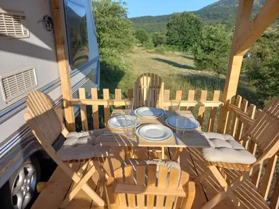 a table and chairs on a porch with a bus at Tomiceva Koliba Rtanj 2 in Rtanj