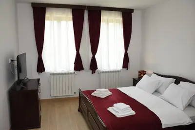 a bedroom with a bed and two windows with red curtains at Kod Bogdanovica in Vrtovac