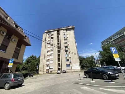 a parking lot with cars parked in front of a tall building at Apartman Lea in Paraćin